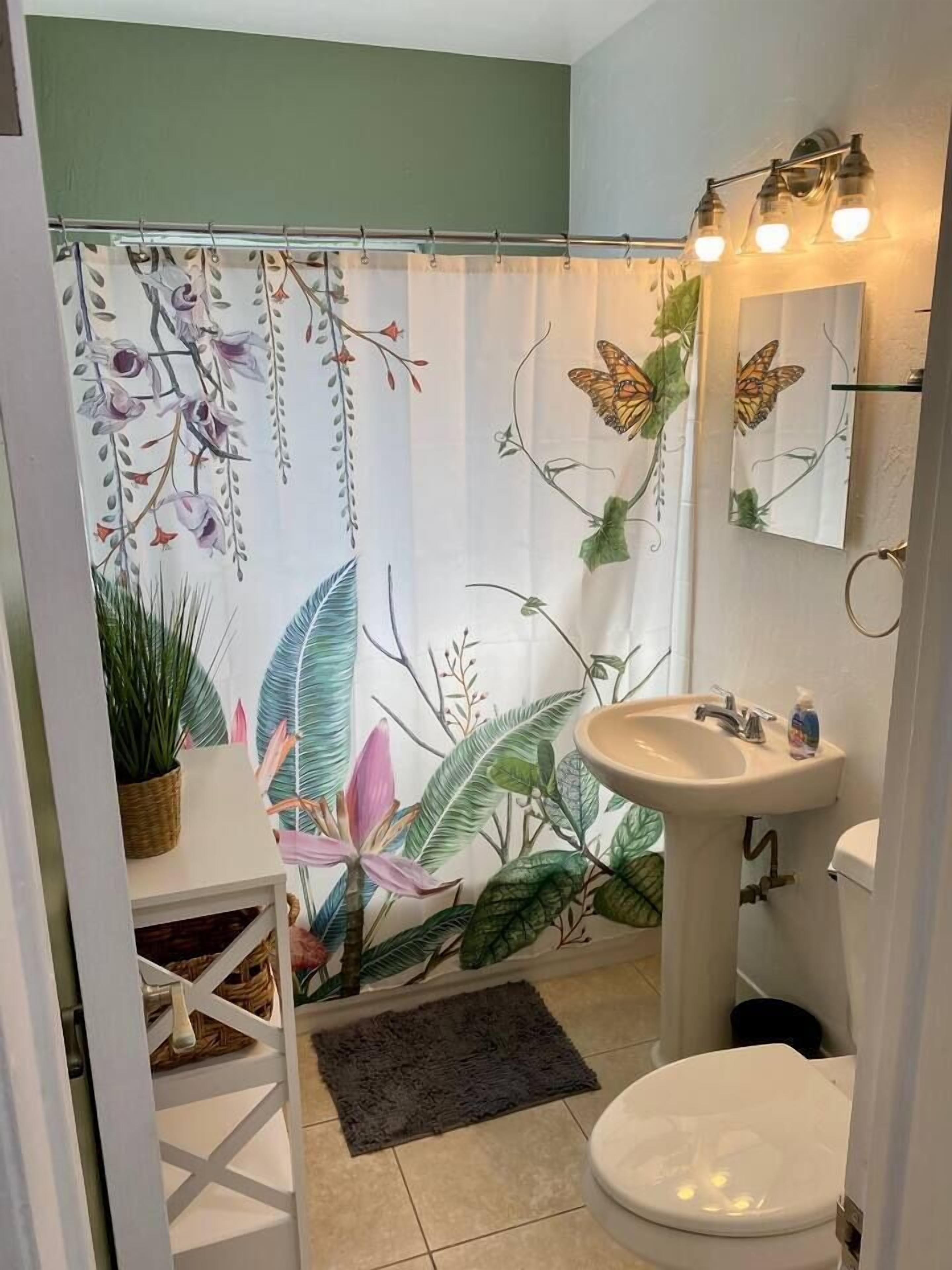 Ein Badezimmer mit Duschvorhang mit floralen und Schmetterlingsmotiven, einem Waschbecken mit Spiegel darüber und einer Toilette.