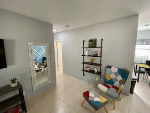 A living room with a sofa, a coffee table, a bookshelf, and a decorative mirror. - Spacious 1BR, Central AC, Real Desk & Office Chair (Fort Lauderdale)