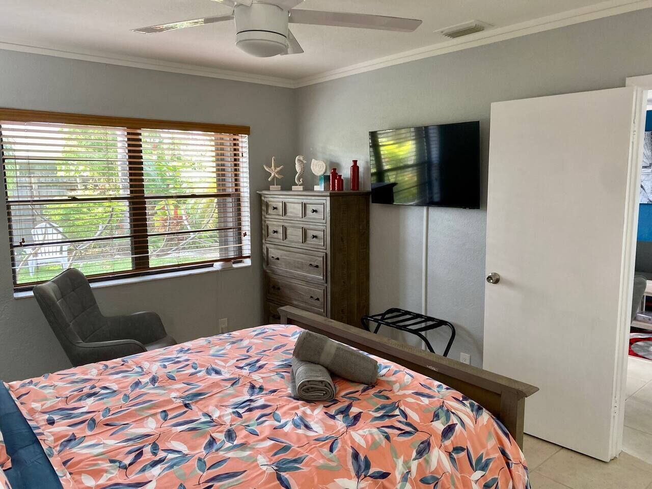Ein Schlafzimmer mit Bett, Kommode, Fernseher und einem Fenster mit Jalousien.