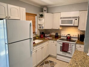 A kitchen with white cabinets, a refrigerator, a microwave, a stove, and a sink.