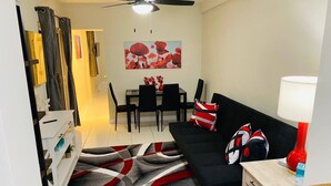Ein modernes Wohnzimmer mit einem schwarzen Sofa, einem Esstisch mit Stühlen und einer roten Lampe.