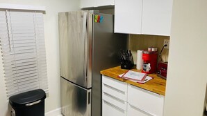 Eine kleine Küche mit einem Edelstahl-Kühlschrank, weißen Schränken, einer Holz Arbeitsplatte und einem schwarzen Mülleimer.