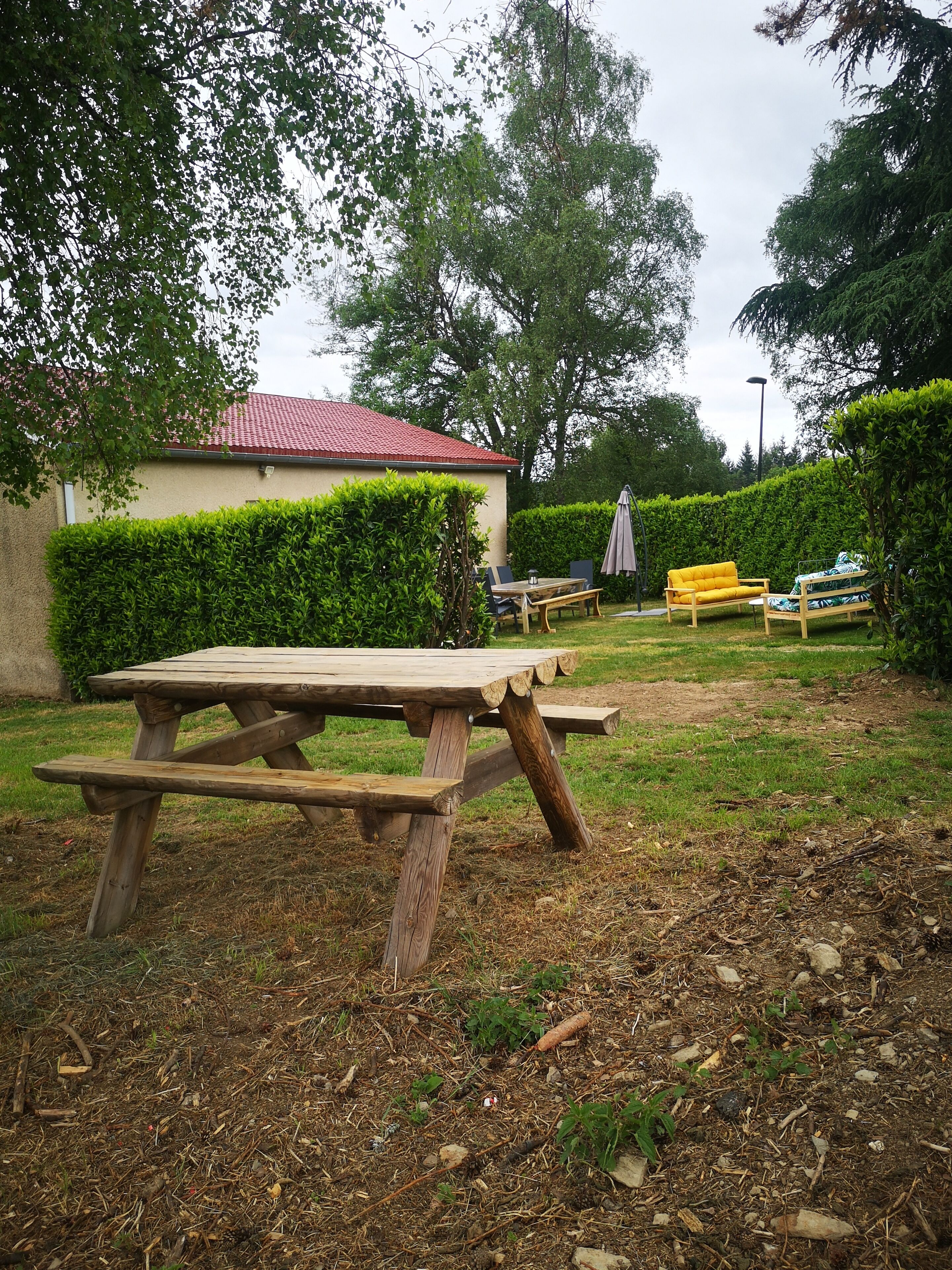 Une table de pique-nique en bois, située dans un espace herbeux, avec un bâtiment en arrière-plan.