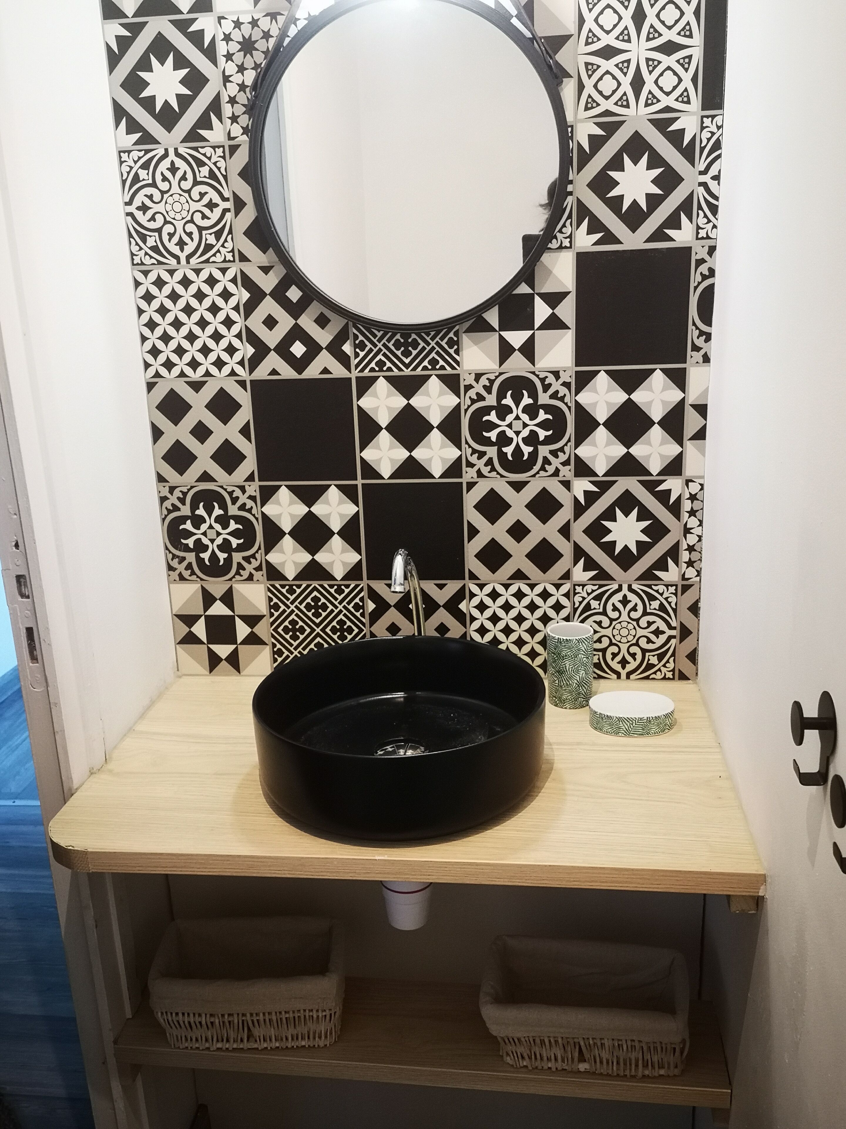A bathroom with a black sink, a round mirror, and patterned tiles.