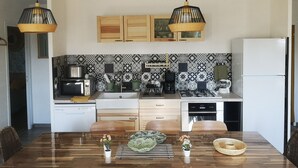 A modern kitchen with a wooden dining table, two hanging pendant lights, a refrigerator, and a patterned backsplash.