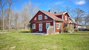 A red wooden house with a white door and windows, surrounded by a grassy yard and trees. - Gorgeous home in åryd with kitchen (Åryd)