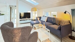 Ein modernes Wohnzimmer mit grauem Sofa, einem Glastisch und einem Fernseher.