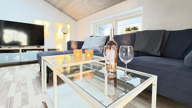Ein modernes Wohnzimmer mit einem Glastisch, einer Couch, einem Fernseher und einem Fenster mit Pflanzen.