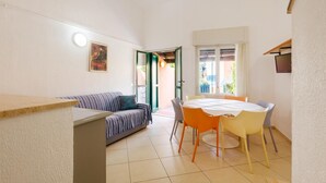 Un espace de vie compact comprenant un canapé, une table à manger avec des chaises, et une vue sur un espace extérieur accessible par une porte ouverte.