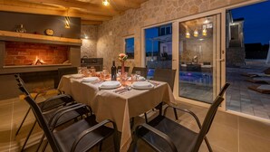 An outdoor dining area with a stone wall, a brick fireplace, and a view of the pool.