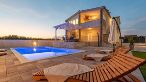 A two-story house with a swimming pool, outdoor seating, and a covered patio area.