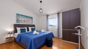 A neatly arranged bedroom with a bed, a painting, a bedside lamp, and a view of the outdoors.