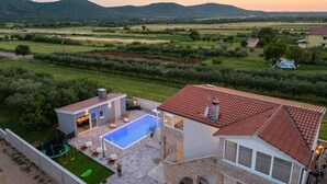 A modern house with a swimming pool, a patio with outdoor furniture, and a view of the surrounding countryside.