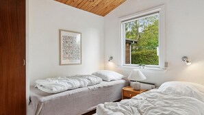 Une chambre avec deux lits, une fenêtre donnant sur un paysage verdoyant, un luminaire fixé au mur et un tableau encadré.