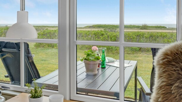 Ein Zimmer mit großem Fenster und Blick auf ein Wiesfeld und den Strand.