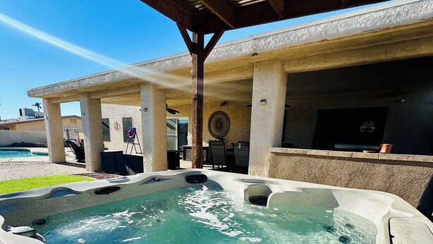 Ein Whirlpool unter einer überdachten Terrasse, im Hintergrund ein Schwimmbecken.