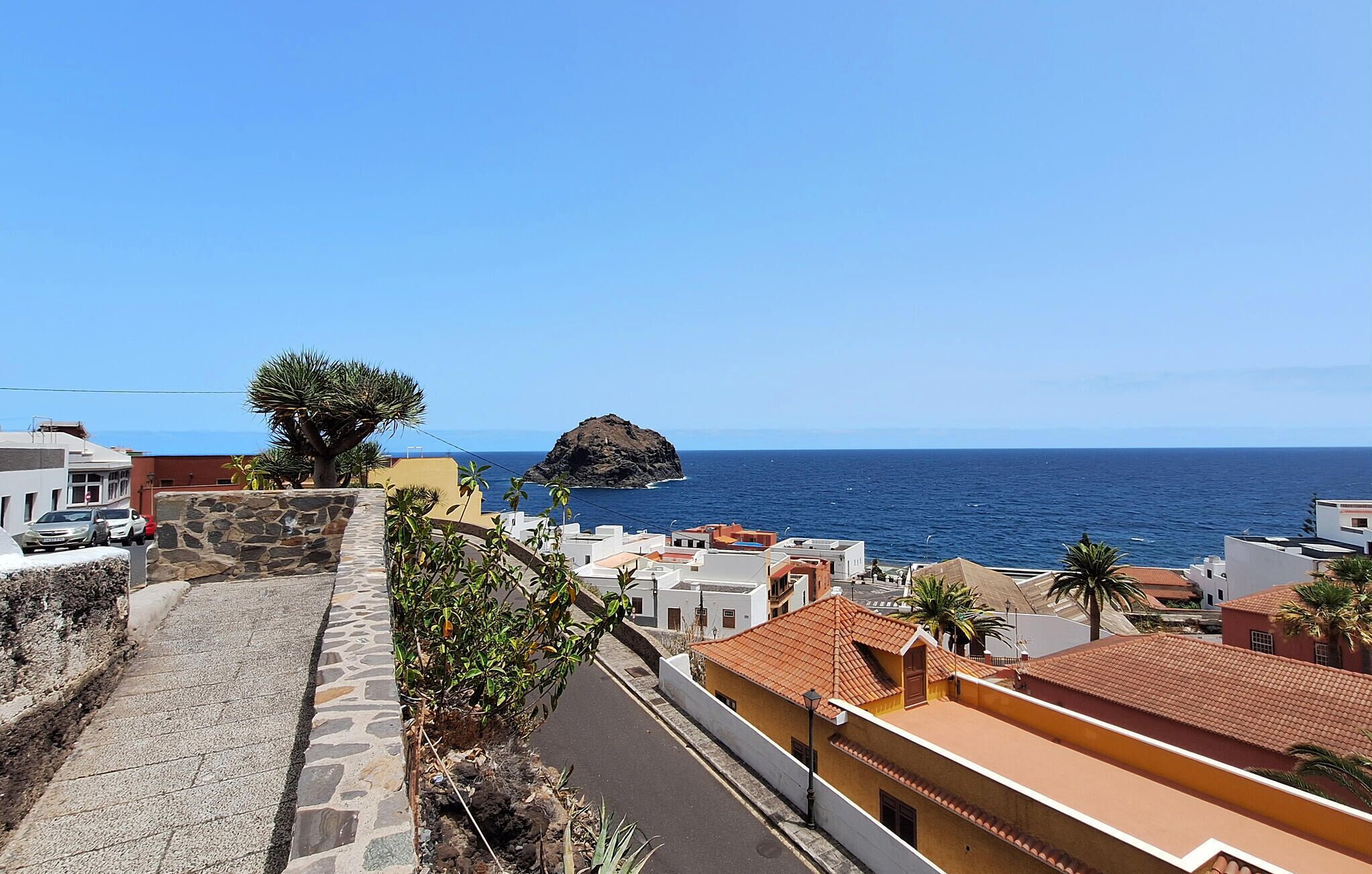 Un pueblo costero con calles empedradas de piedra, edificios con tejados de tejas rojas y un prominente saliente rocoso en el mar.