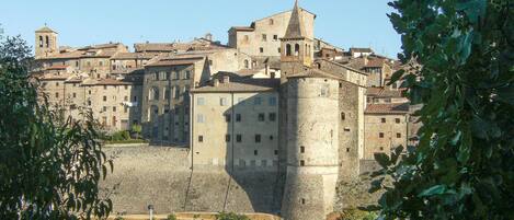 Un edificio histórico de piedra con varios niveles, una torre destacada y una muralla fortificada.