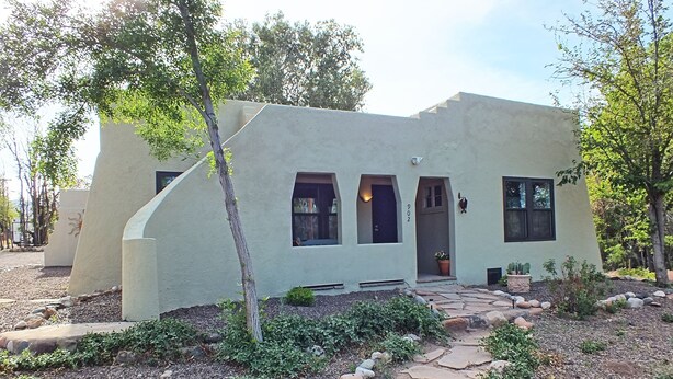 Una casa moderna con un diseño arquitectónico único, que presenta una fachada curva, múltiples ventanas y un camino de piedra que conduce a la entrada.