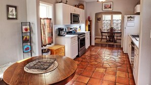 Cocina compacta con armarios blancos, microondas, estufa y comedor con mesa y sillas de madera.