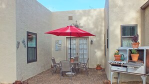 Un patio con mesa y sillas, un paraguas rojo y una estufa antigua.