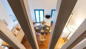 A dining area with a round table and chairs, a television on a cabinet, and a view of the kitchen through an open door.