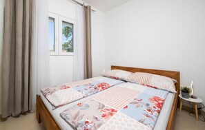 Un dormitorio con una cama de madera, ropa de cama floral, una ventana con cortinas y una mesita de noche con una planta.
