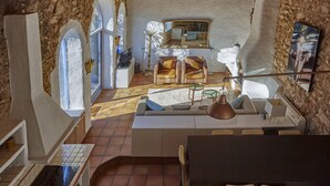 A spacious living area with a large sofa, a coffee table, and a dining table. There are two chairs, a lamp, and a TV mounted on the wall. - Casa Azul  at Masia Nur Sitges (Adults only 18+) (Canyelles)