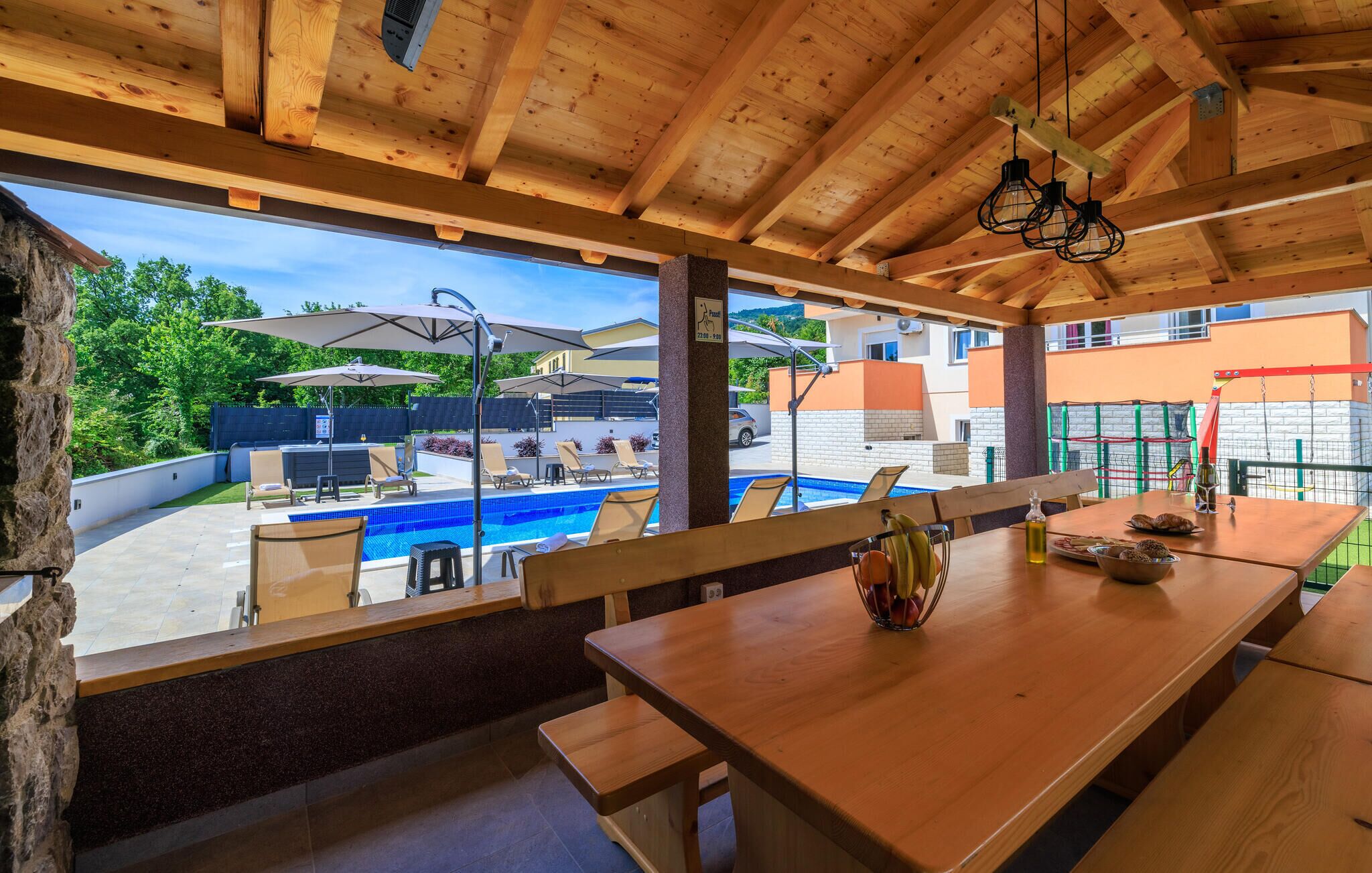 A wooden deck with a pool, lounge chairs, and a table with food and drinks.