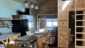 A cozy cabin interior with a wooden dining table, chairs, a kitchen area, and a loft bedroom. -  Modern Cabin to relax and unwind  (Au train)