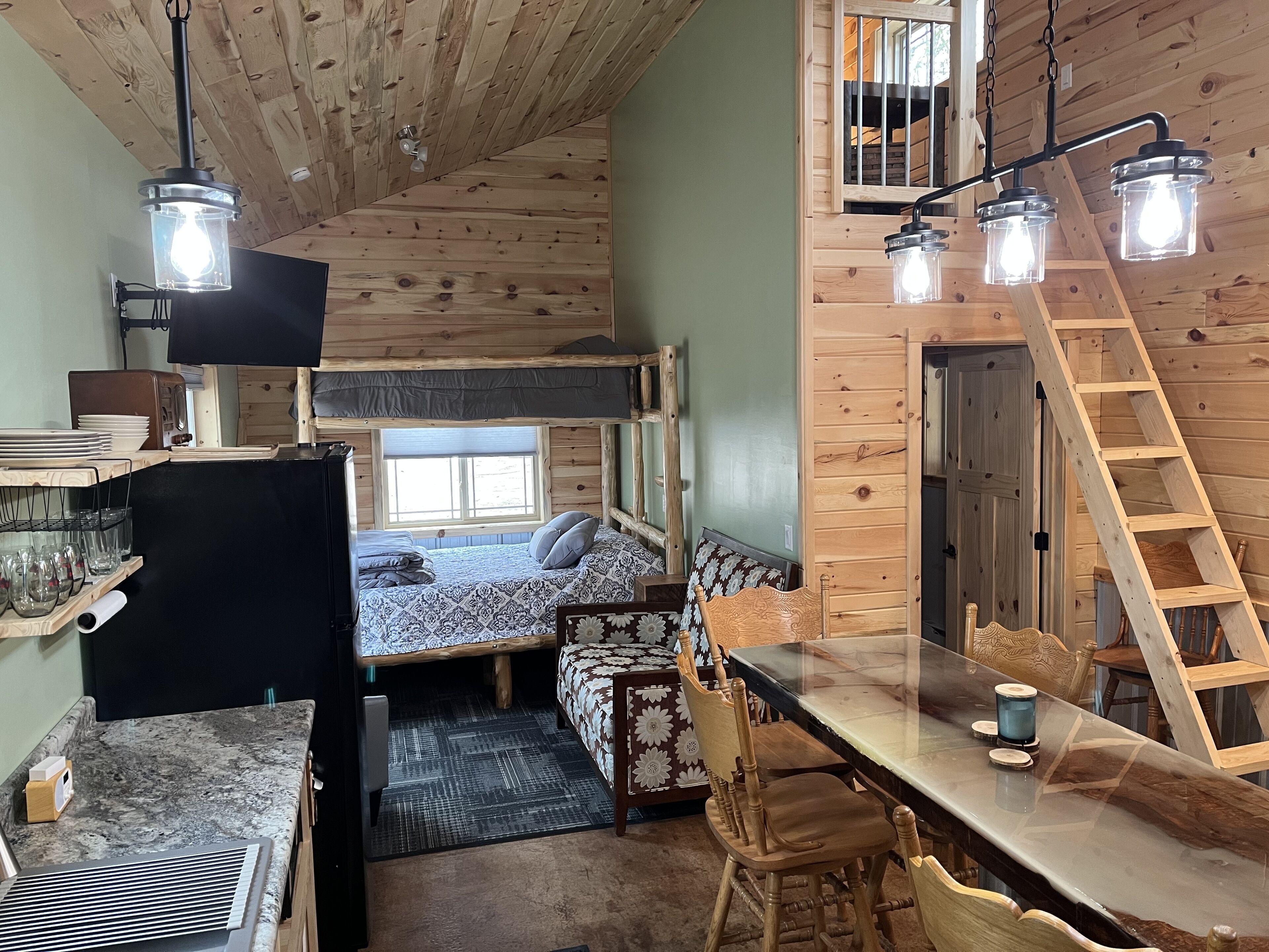 Een knus kamer in chaletstijl met een stapelbed, een eettafel met stoelen, en een ladder naar het bovenste bed.
