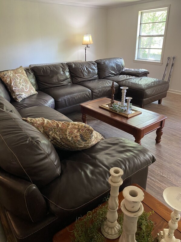 A living room with a brown leather sectional sofa, a wooden coffee table, and decorative items. - 3 bedroom 2 bath Historic Home (Summit)