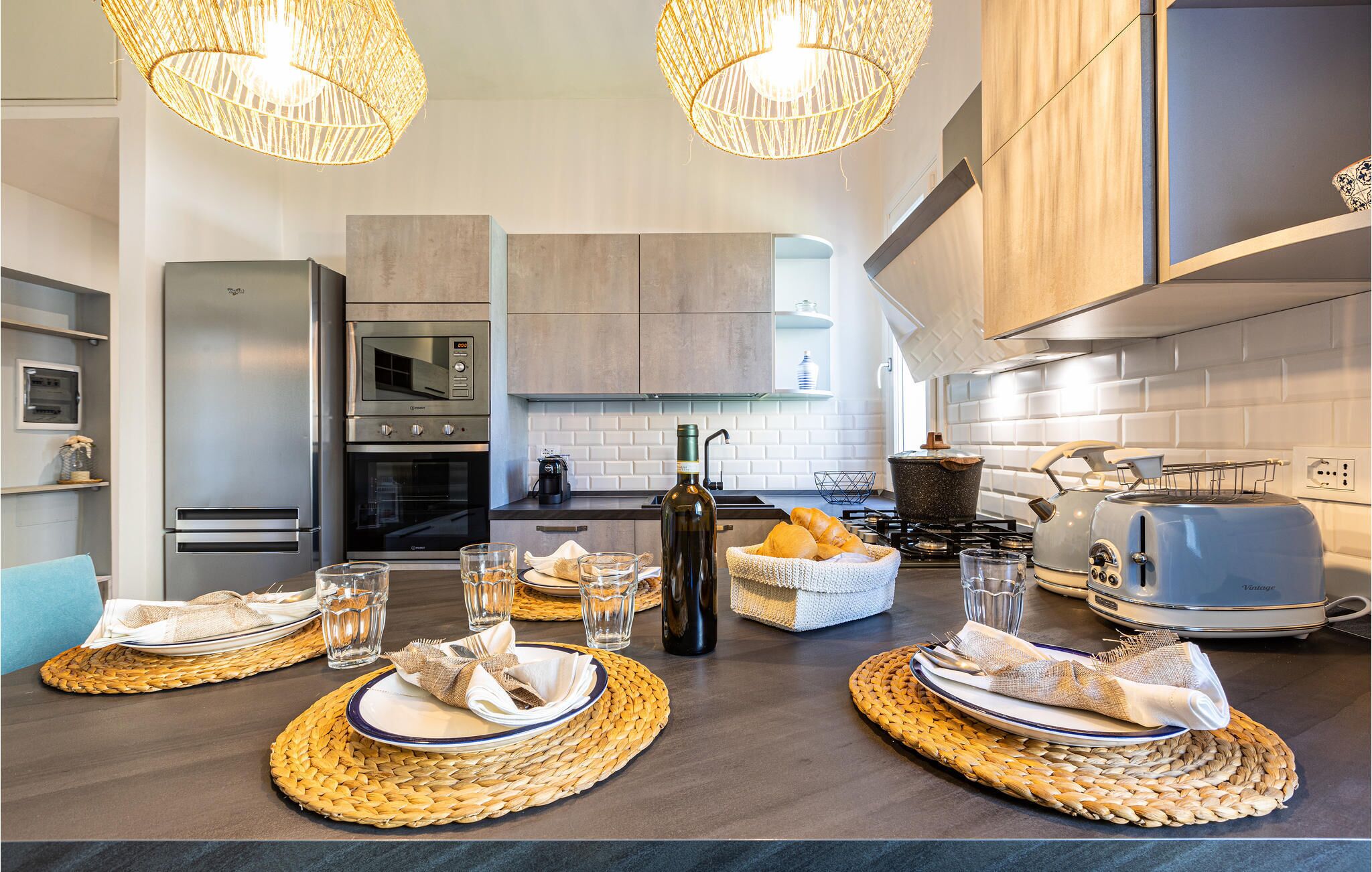 A modern kitchen with stainless steel appliances, a dining area with woven placemats, and a coffee maker.