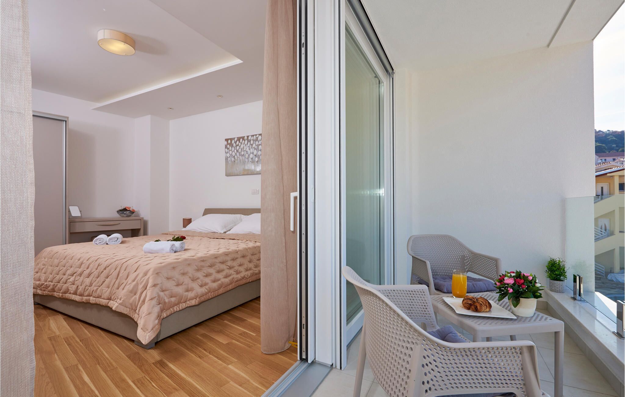 A hotel room with a bed, a small table with breakfast items, a chair, and a balcony with a view.