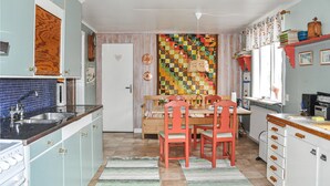 Une cuisine avec une table à manger, des chaises et une courtepointe colorée accrochée au mur.