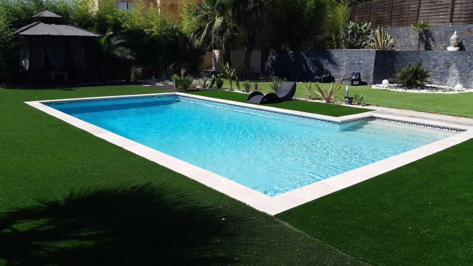 A rectangular swimming pool with a white border, surrounded by artificial green grass.