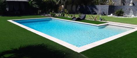 A rectangular swimming pool with a white border, surrounded by artificial green grass.