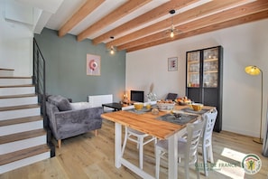 A modern living room with a wooden dining table, grey sofa, and a staircase. - L'echappée Belle - Gommenec'h (GOMMENEC'H)