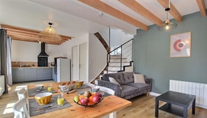 A modern kitchen with a dining area, a grey sofa, and a staircase.