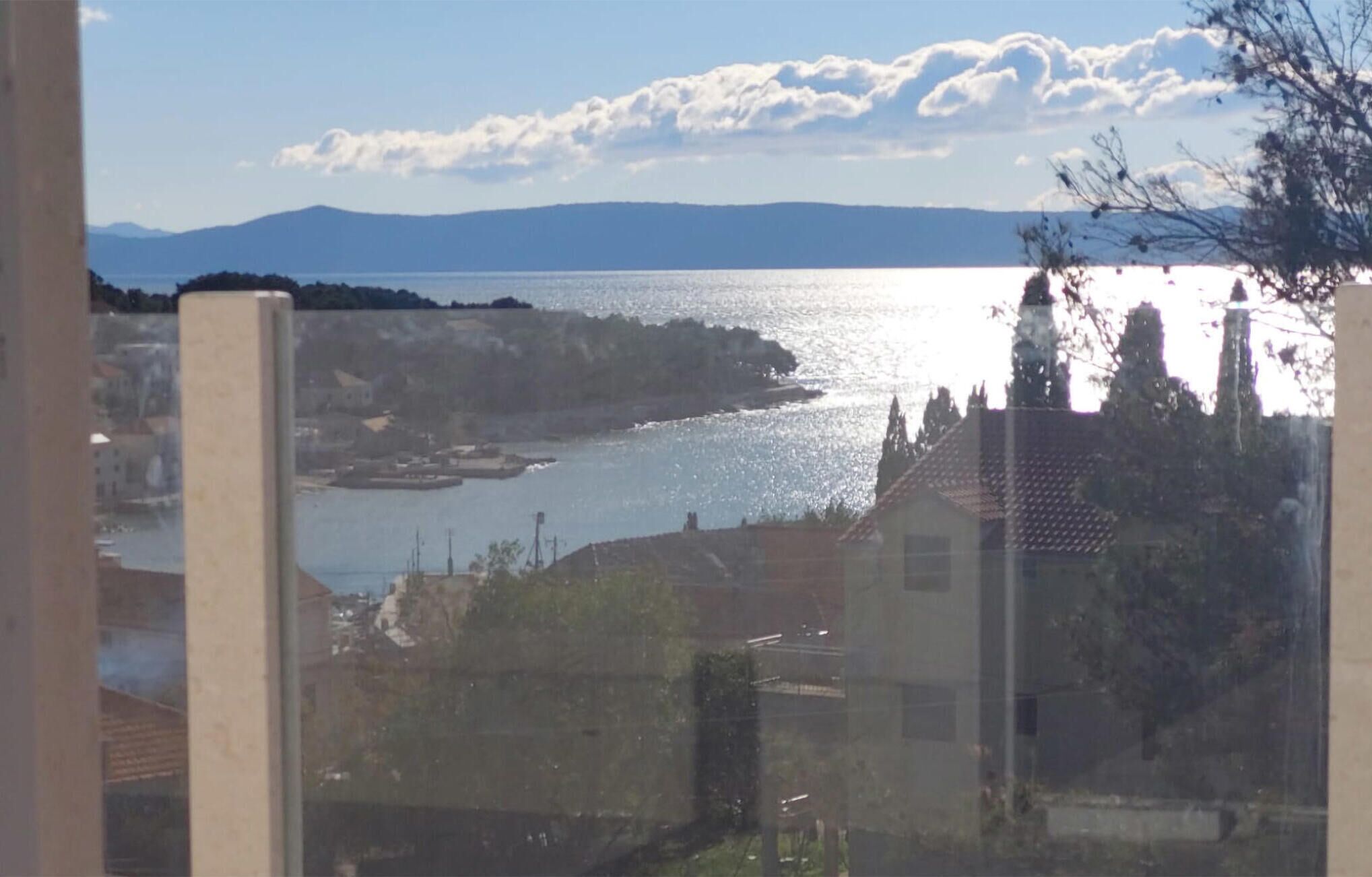 Vista costera con masa de agua, edificios y una cadena montañosa distante.