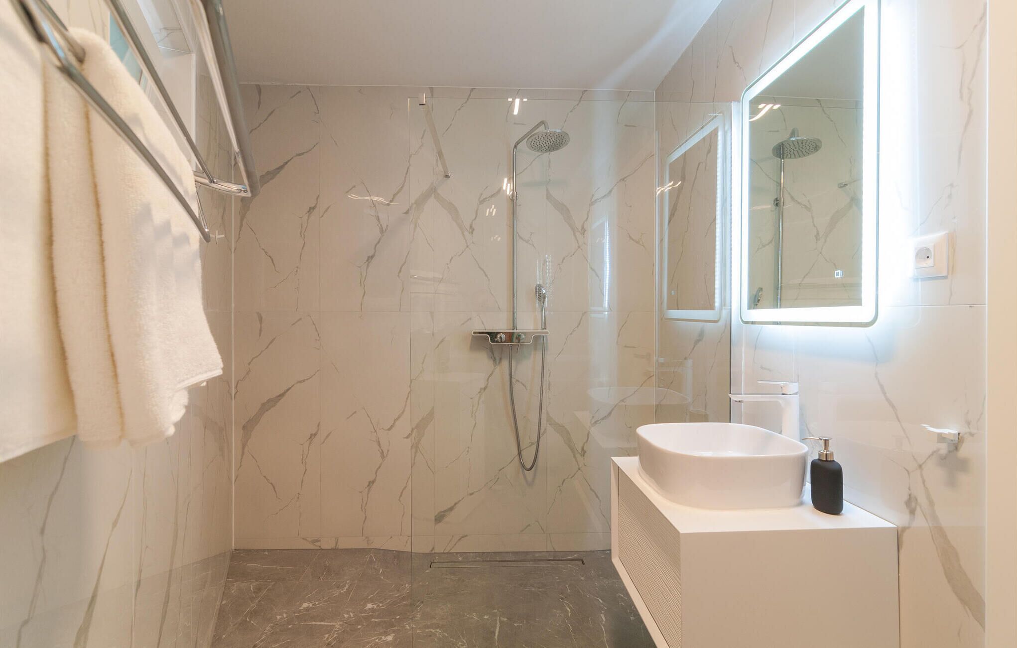A modern bathroom with a glass-enclosed shower, a white sink, and a large mirror.