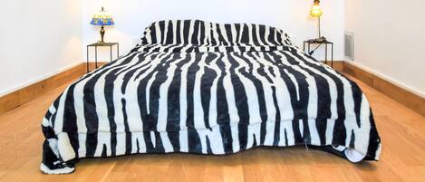 A bed with a zebra-striped duvet in a room with wooden flooring and two bedside lamps.