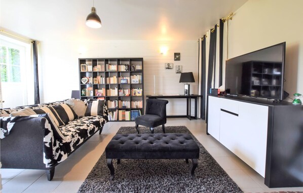 En moderne stue med en sofa i sort og hvidt mønster, en sort lænestol, en knapbetrukken skammel, en reol fyldt med bøger, et fladskærms TV og et skrivebord med en lampe.