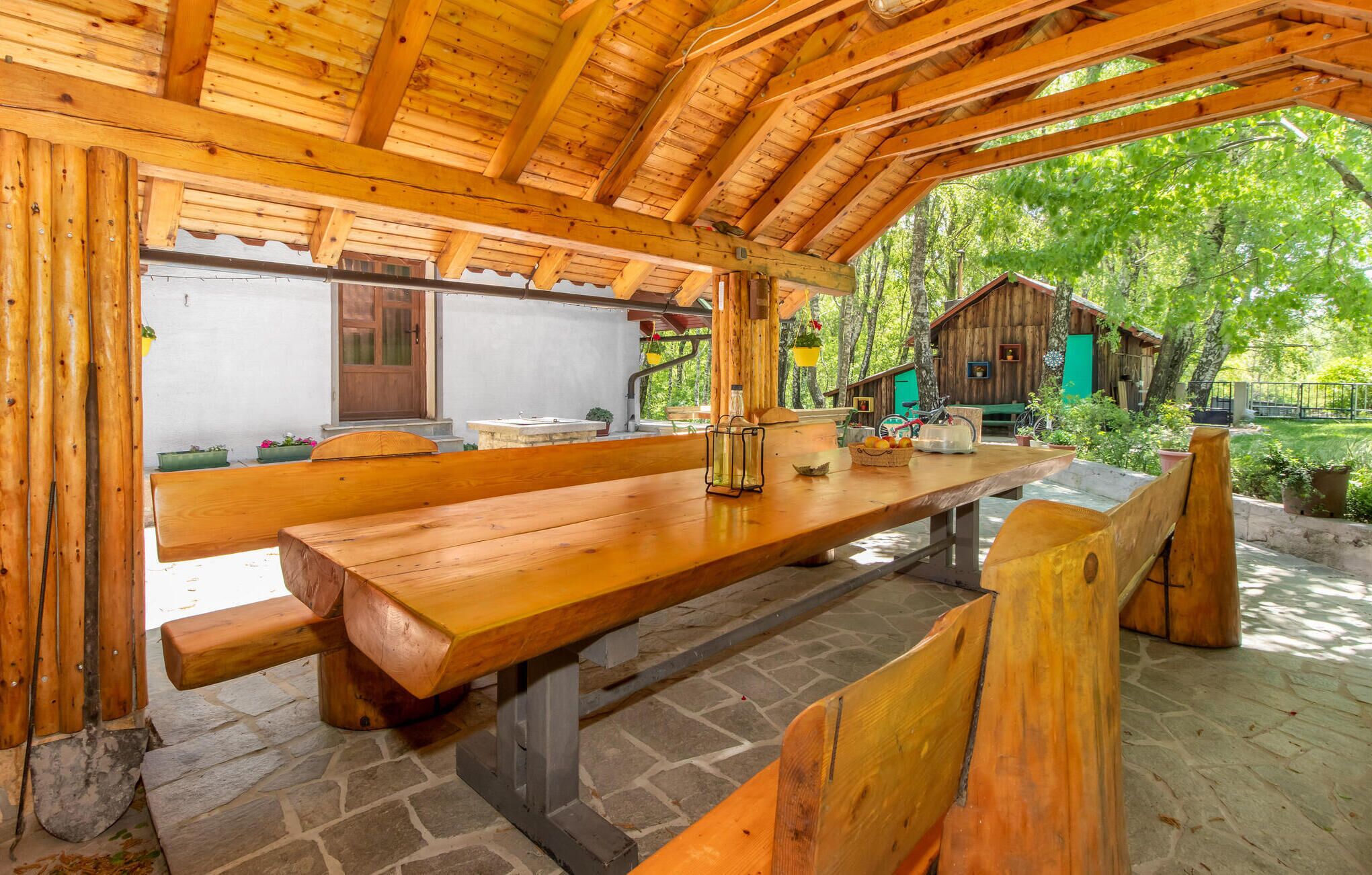 Un pabellón rústico de madera con suelo de piedra, un banco de madera y una mesa de picnic.