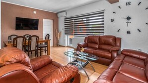 A living room with leather sofas, a glass coffee table, a TV on the wall, and a large clock.
