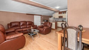 A living room with a brown leather sofa, a glass coffee table, and a dining area with a wooden table and chairs.
