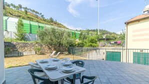 En udendørs patio med et bord dækket til fire personer, omgivet af stenvægge og vegetation.