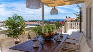 A wooden table set with cups and a fruit bowl, under a pergola with hanging lights, overlooking a scenic view of houses and mountains. - Stunning home in Sumartin (Sumartin)