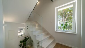 A modern staircase with glass railings, a potted plant, and a window with a view of trees. - Stunning home in Sumartin (Sumartin)