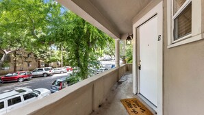 Un portico coperto con una porta bianca con la scritta 'E', un tappetino d'ingresso e vista su auto parcheggiate e alberi.